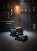 Makita 18V batteri og matchende batteriholder placeret på værkstedsbord med værktøj i baggrunden