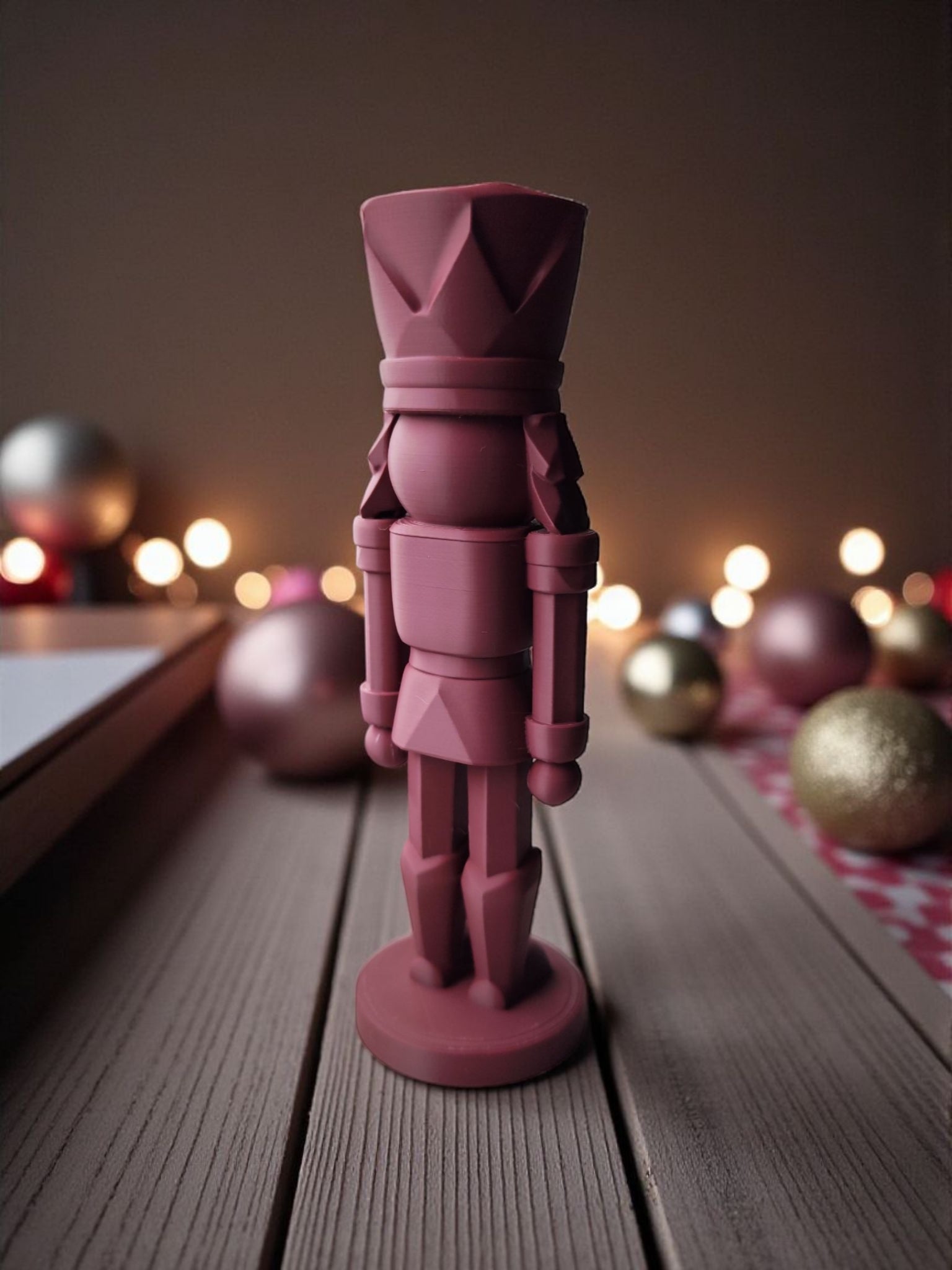 Rød 3D-printet nøddeknækker figur set fra siden med juleornamenter og bokeh-lys i baggrunden.