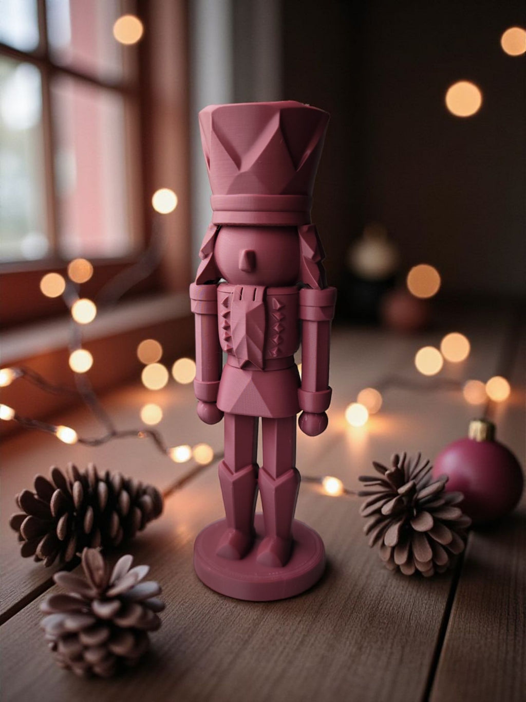 Rød 3D-printet nøddeknækker figur stående på bord med kogler og julepynt, oplyst af varme julelys.