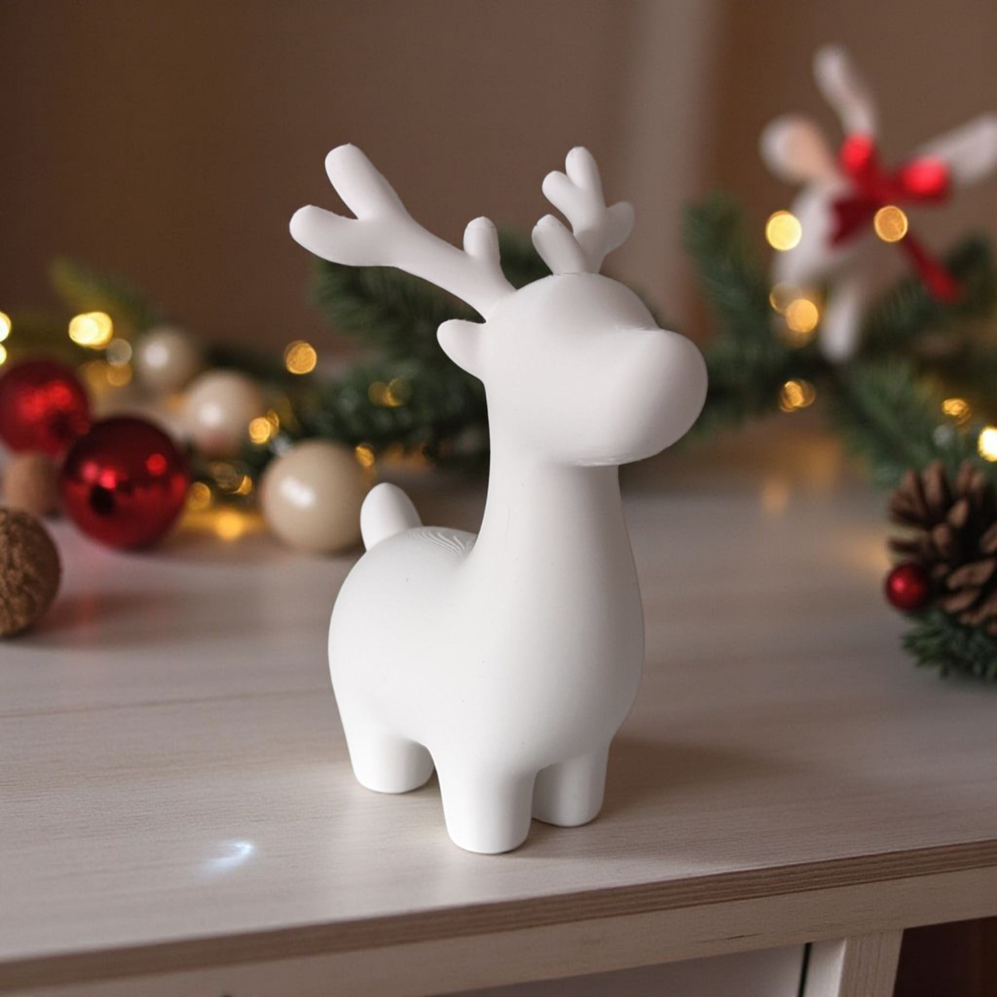 Hvid 3D printet rensdyr figur stående på lys træbord med julepynt og lyskæde i baggrunden.