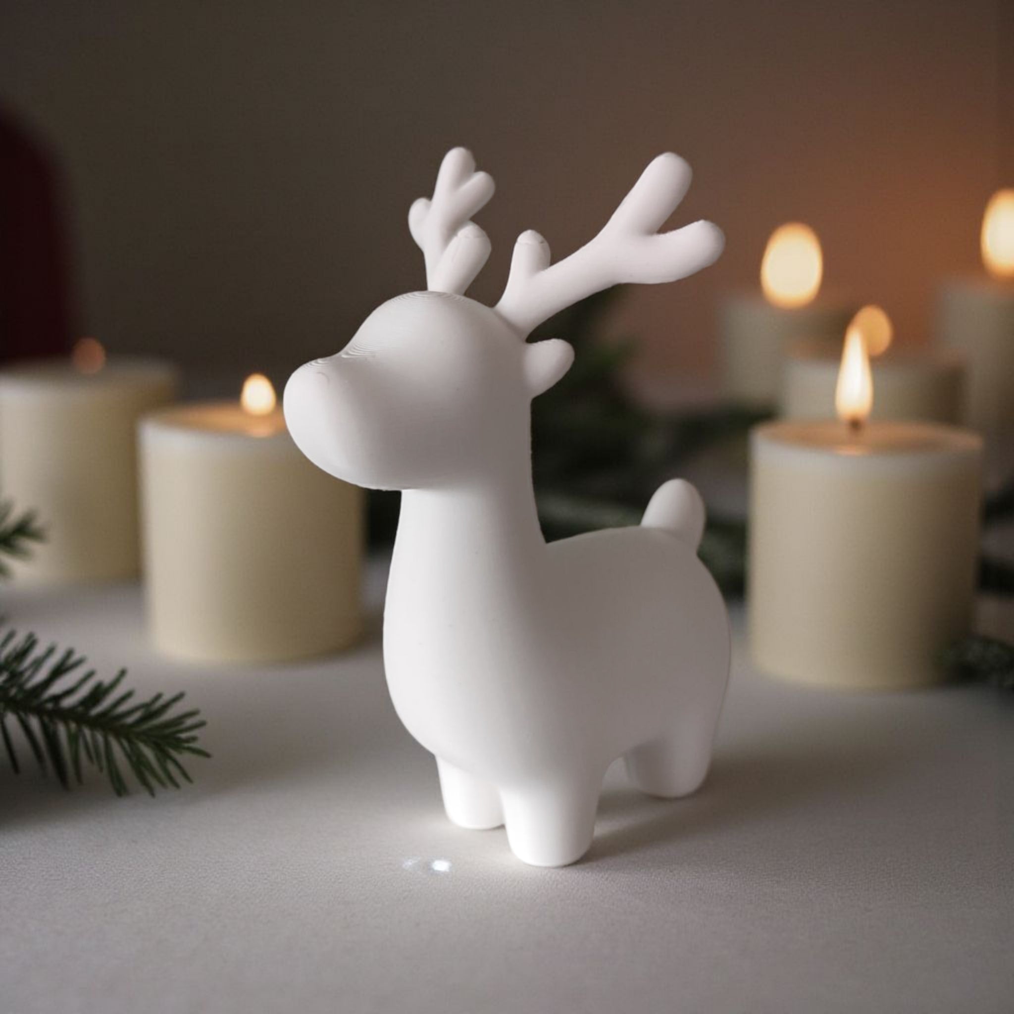 Hvid 3D printet rensdyr figur på bord omgivet af LED stearinlys og gran.