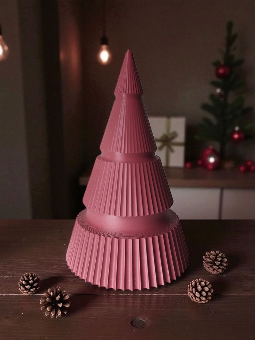 Rødt 3D printet juletræ i moderne riflet design på et bord med kogler og baggrundslys.